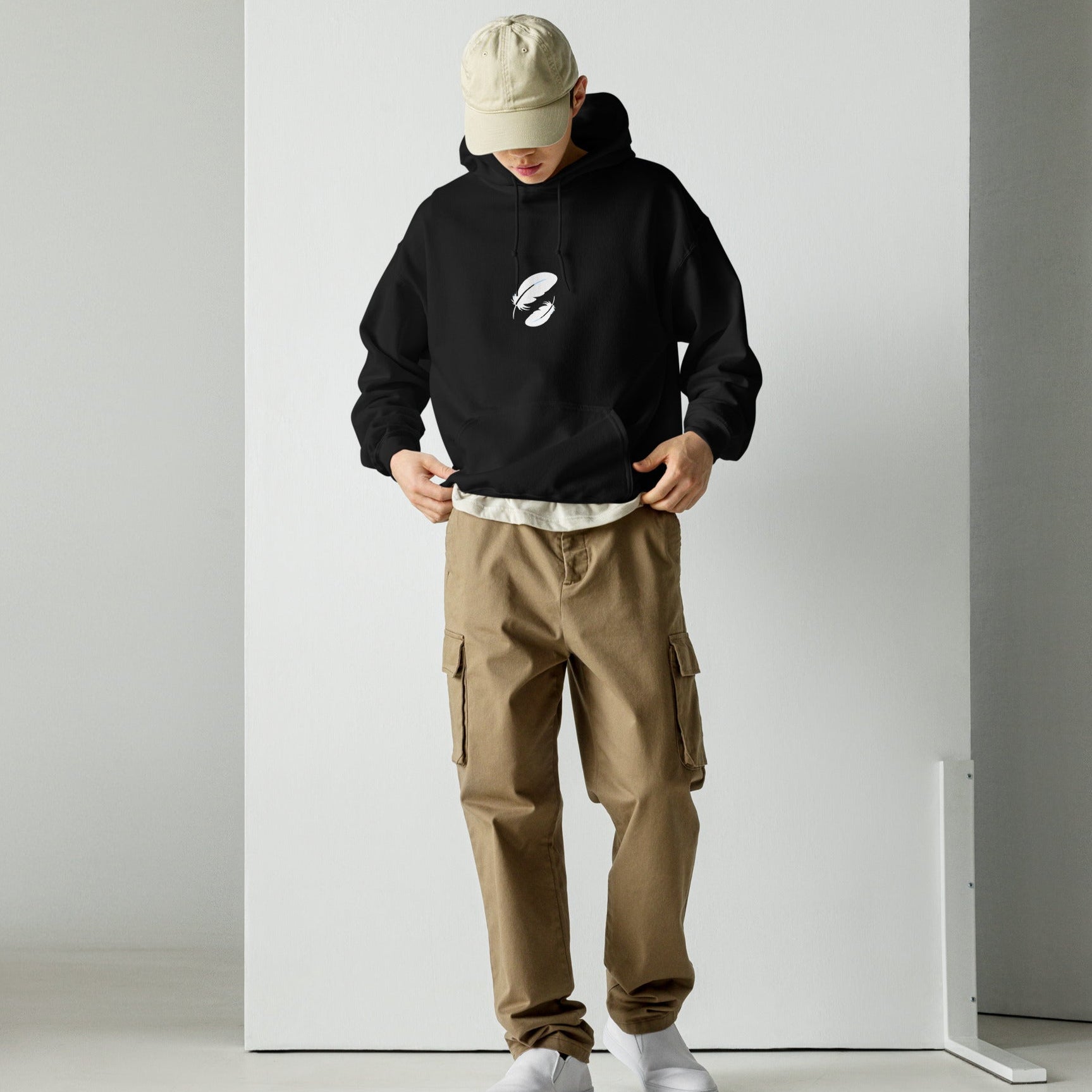 Person wearing a black hoodie, beige cap, and brown cargo pants against a white background