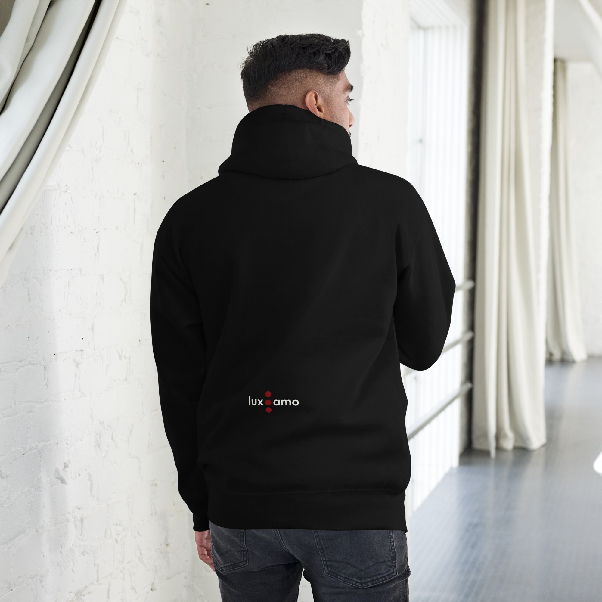 Person wearing a black hoodie with 'lux amo' logo, standing in a room with white curtains.