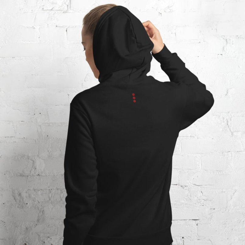 Person wearing a black hoodie with a red logo on the back against a white brick wall.