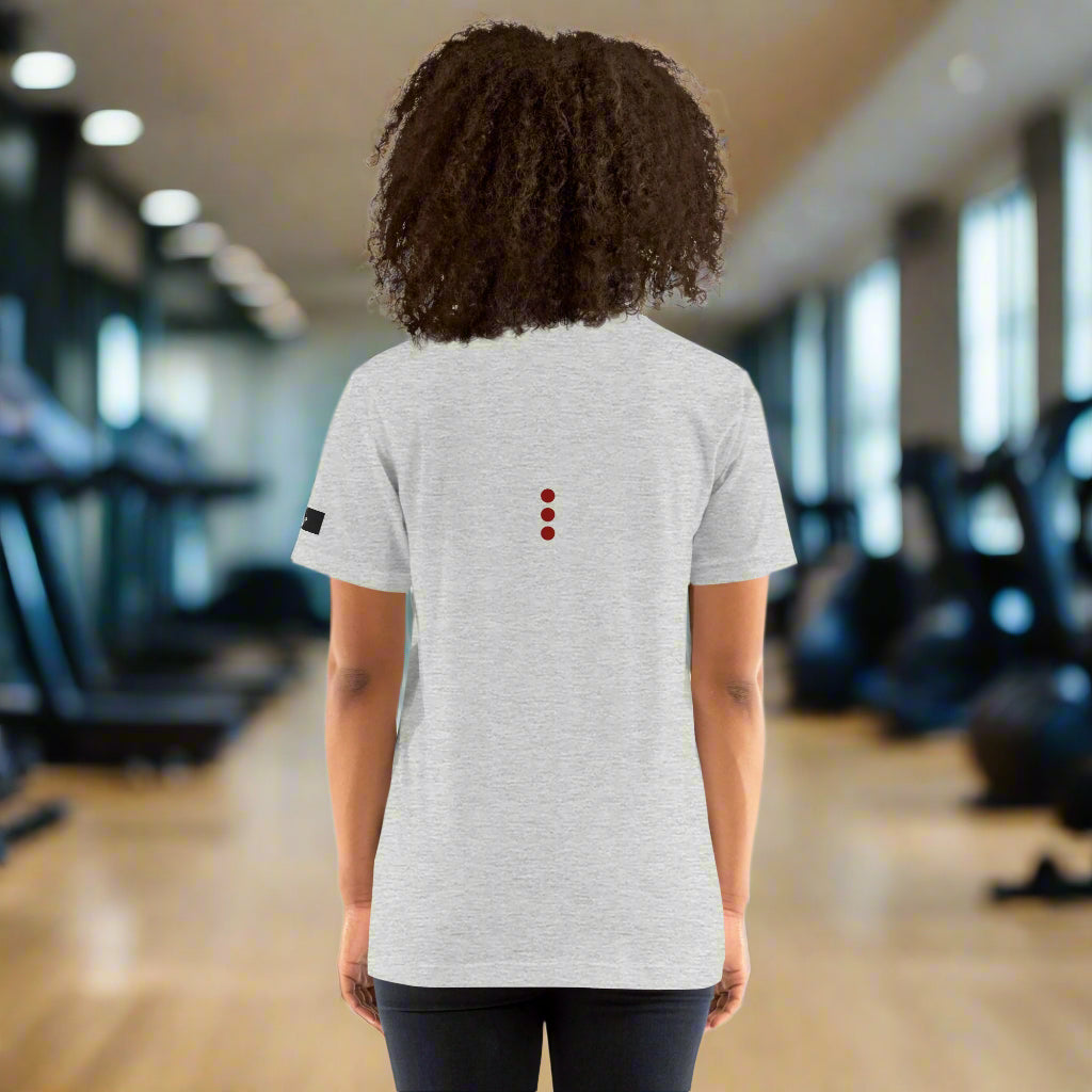 Person wearing a grey t-shirt with a small logo on the back, standing in the gym